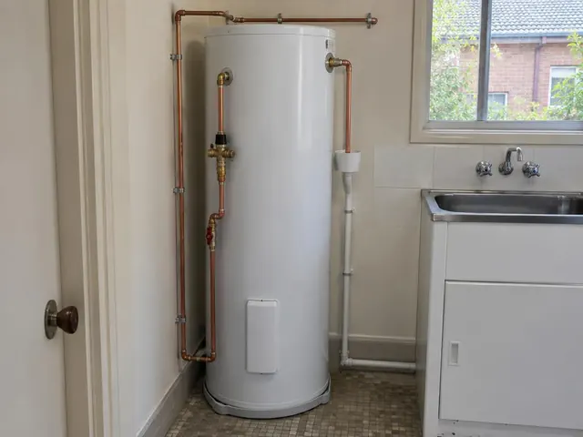 Hot water cylinder beside a laundry sink and tiled wall in Artarmon